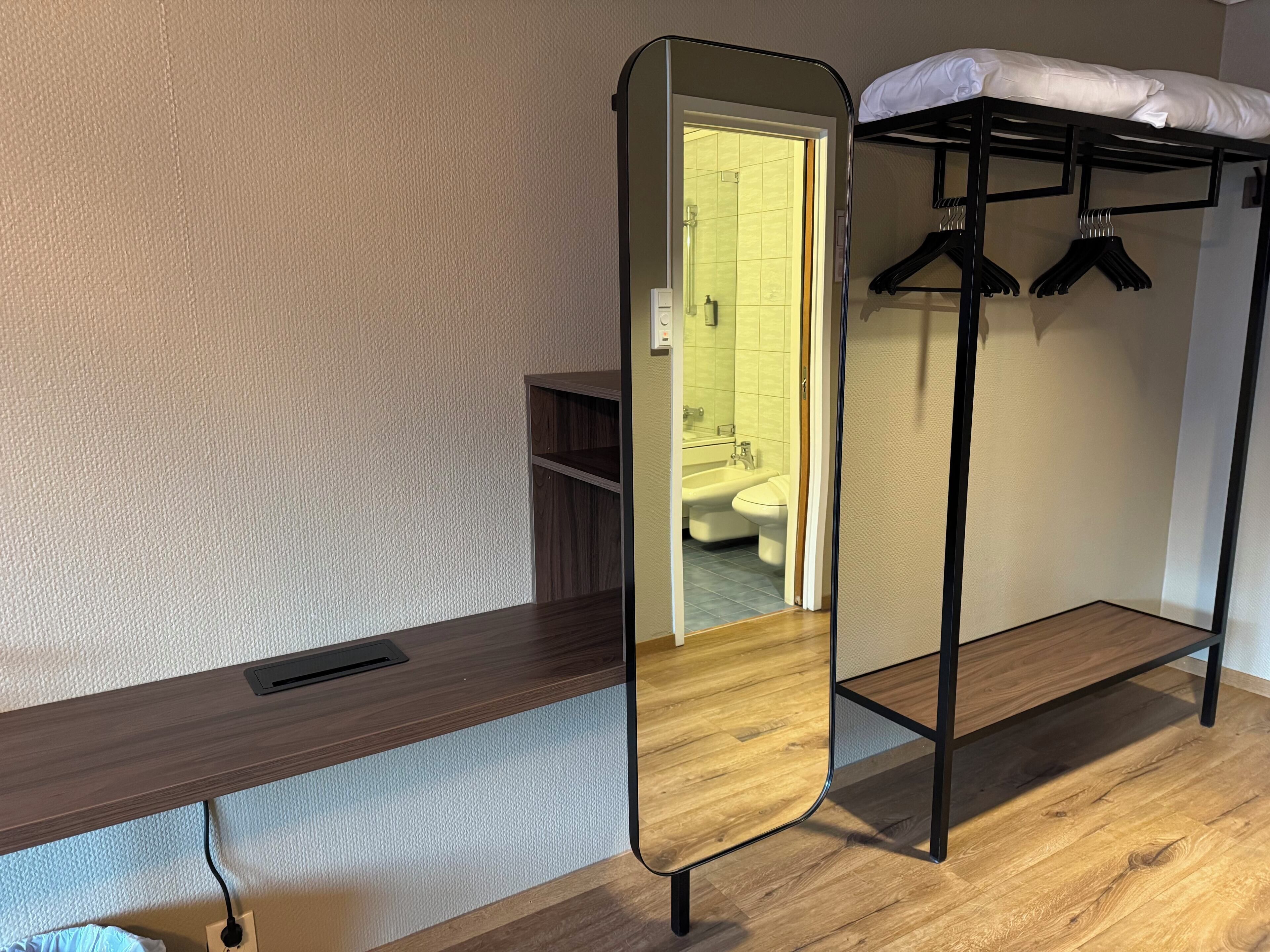 A compact room with a bunk bed, a mirror, a wooden desk, and a bathroom visible through an open door.