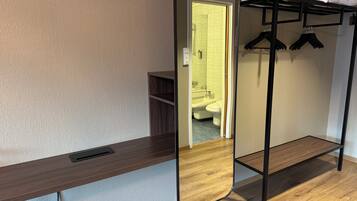 A compact room with a bunk bed, a mirror, a wooden desk, and a bathroom visible through an open door.