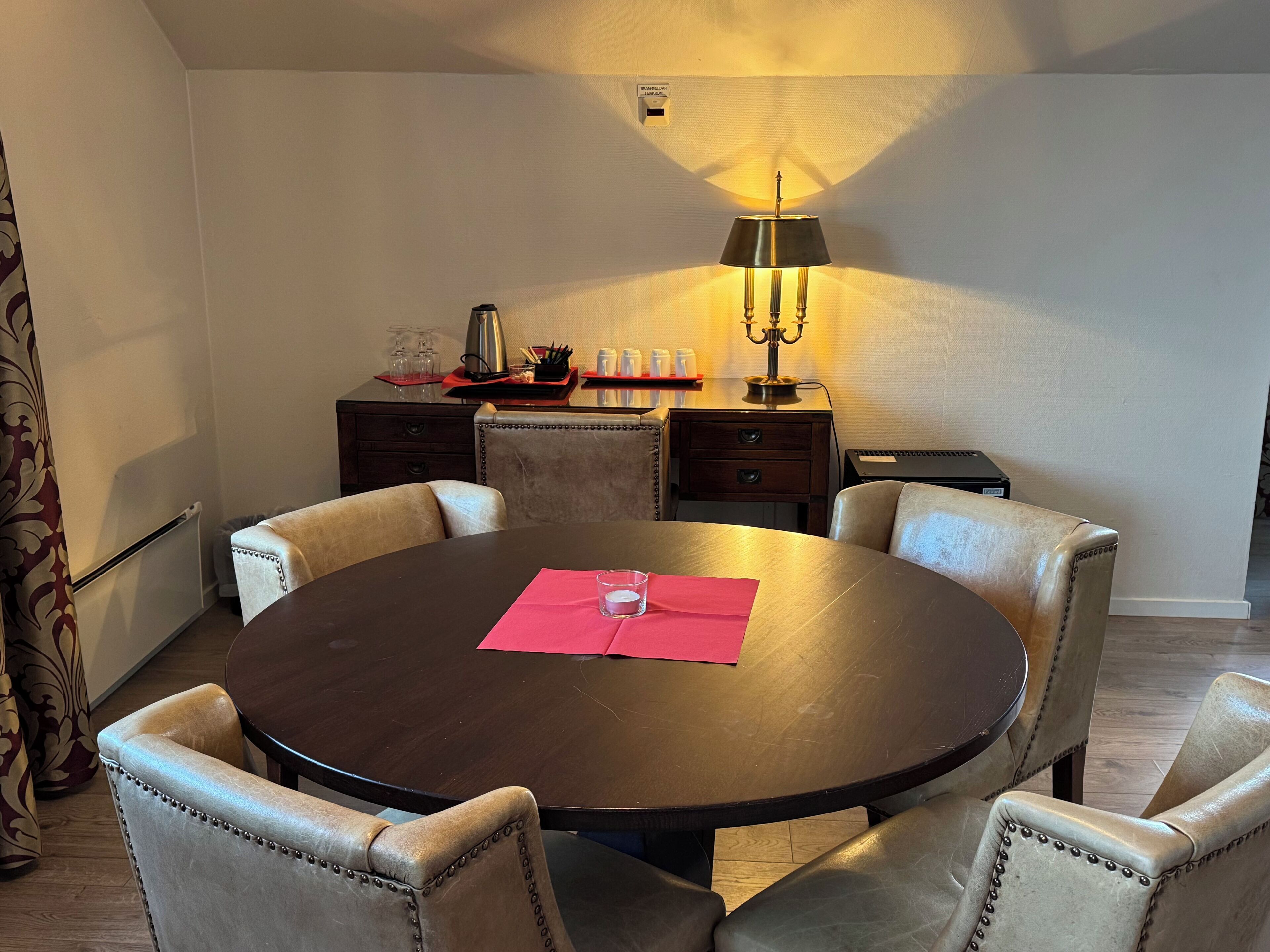 Un coin repas comprenant une table ronde, six chaises rembourrées, une lampe de table et une petite table d’appoint avec des verres et des condiments.