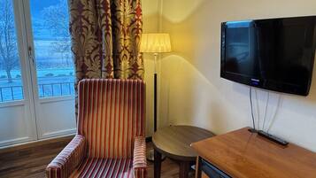 A hotel room with a striped armchair, a small wooden table, a lamp, and a mounted TV.