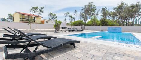 A pool area with lounge chairs and a small building in the background.