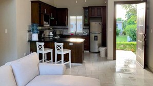 A modern kitchen with dark wooden cabinets, a white countertop, and a built-in refrigerator. There is a white ceiling fan, a water dispenser, and a small trash bin. - Come have Fun in DR! (Sosúa)