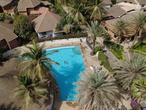 Ett bostadsområde med en swimmingpool omgiven av palmer och hus med tegeltak.