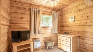 A wooden cabin room with a television, a small heater, a pet bed, and a wooden dresser.