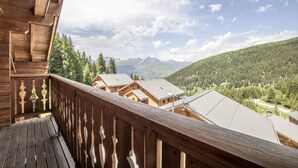 A wooden balcony with a view of a mountain landscape and several buildings.