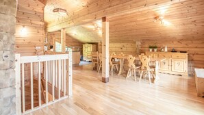 A wooden cabin interior with a dining area, kitchen, and a view of the outside.