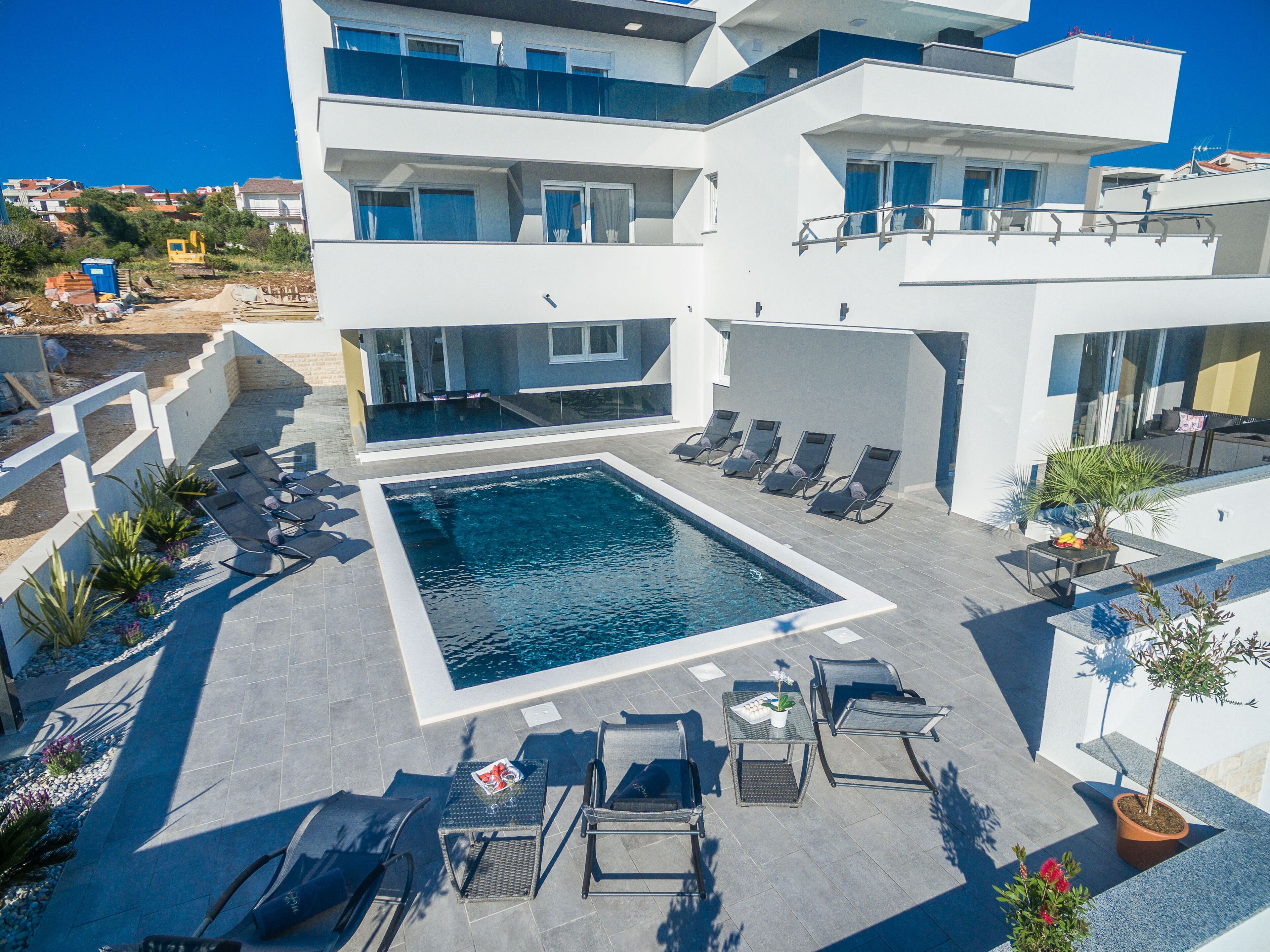 Ein modernes Hotel mit Pool auf dem Dach, Liegestühlen und einem kleinen Tisch mit einer Pflanze.