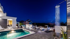 A modern outdoor pool area with a built-in jacuzzi, lounge chairs, and a well-maintained garden. - Villa Magnifica Penthouse with Jacuzzi (Novalja)