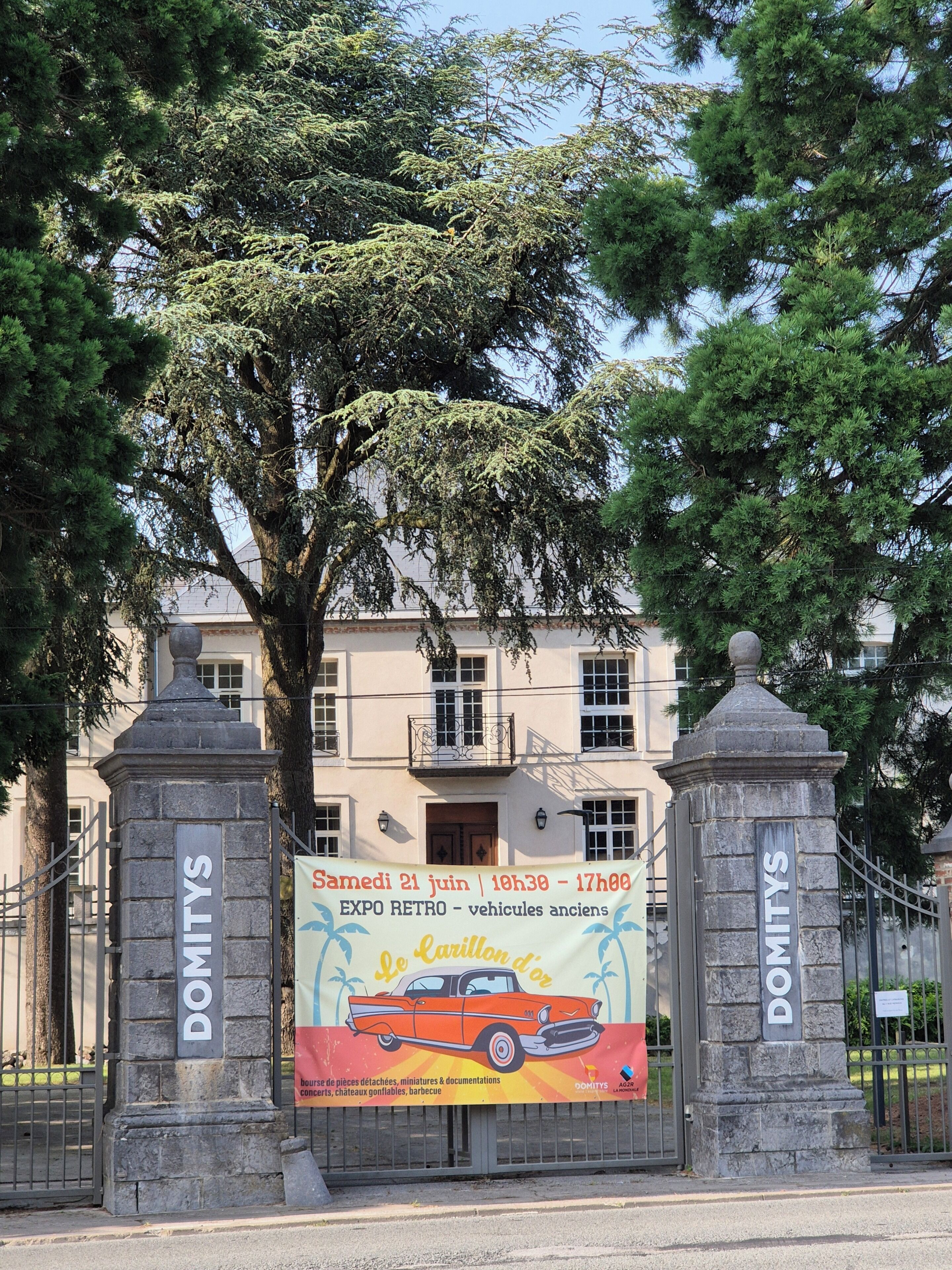 Une entrée d’immeuble avec des panneaux indiquant « DOMITYS », une publicité pour une voiture ancienne et une banderole indiquant la date et l’heure.