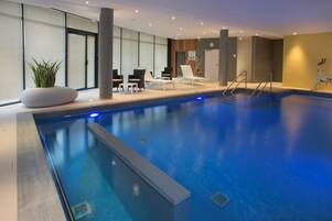 Piscina interior com espreguiçadeiras e um vaso de planta.