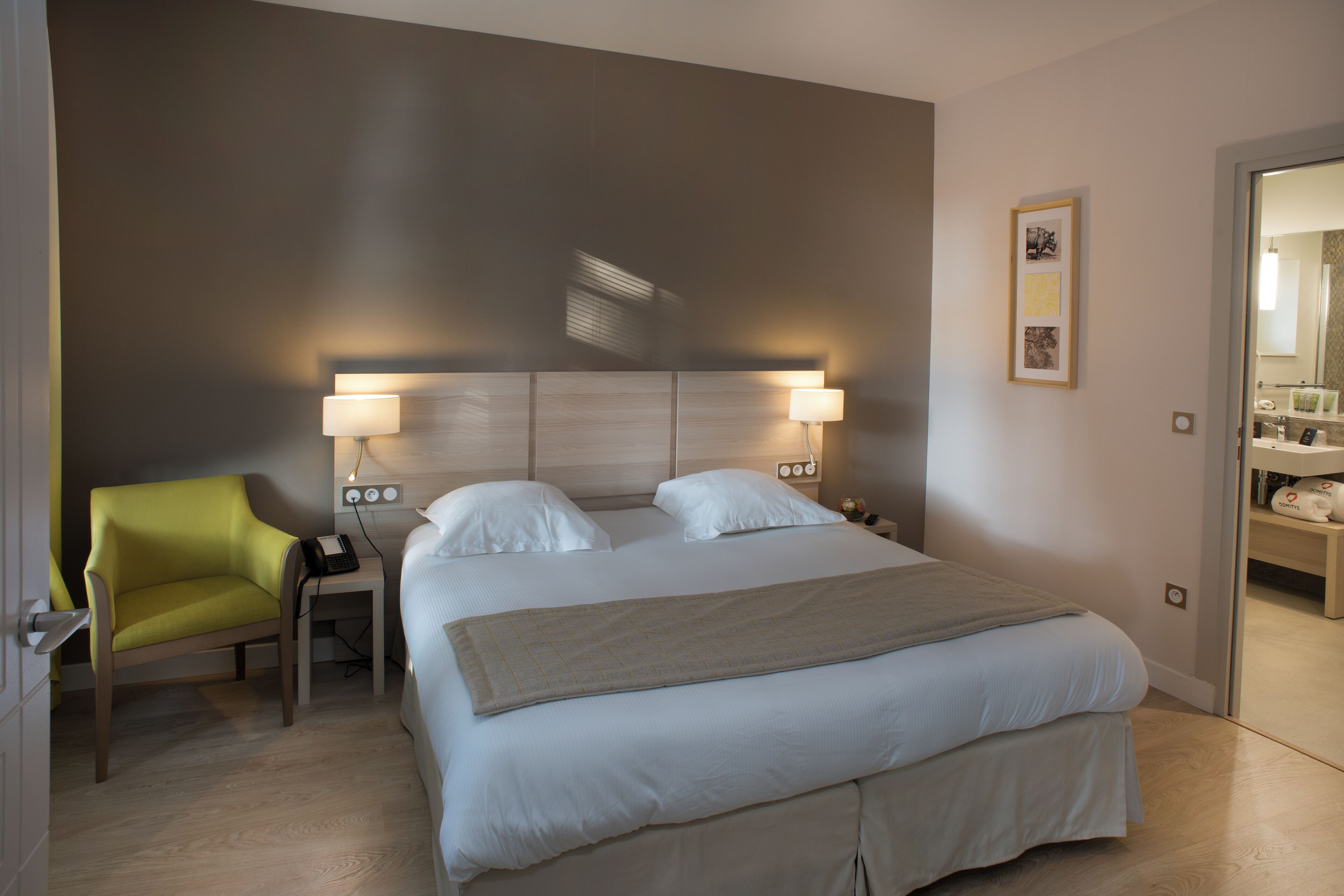Une chambre d’hôtel comprenant un lit, des lampes de chevet, une chaise, une table de chevet avec un téléphone et une porte donnant accès à une salle de bain.