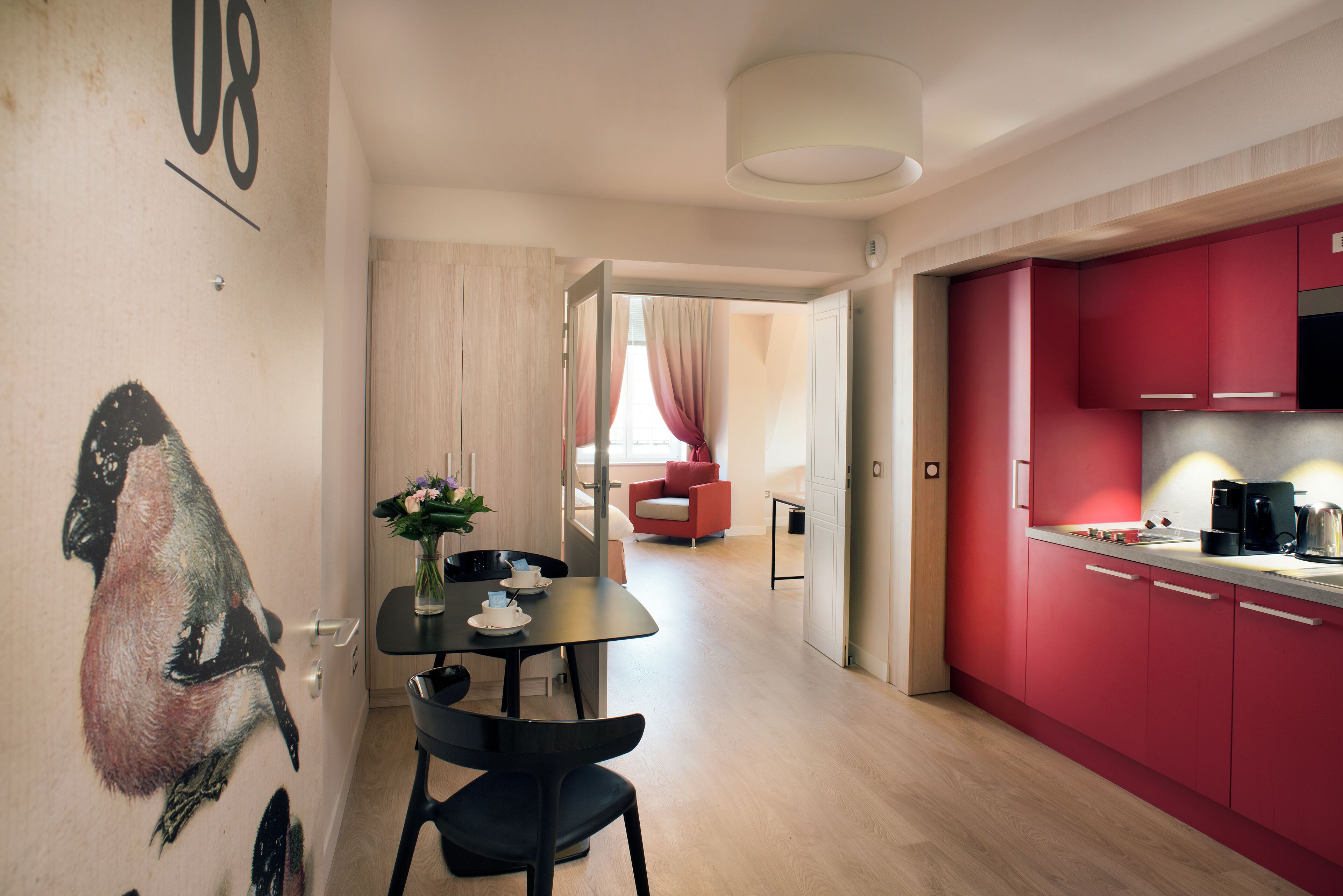 A modern kitchen with red cabinets, a dining area with a table and chairs, and a living space with a red sofa.