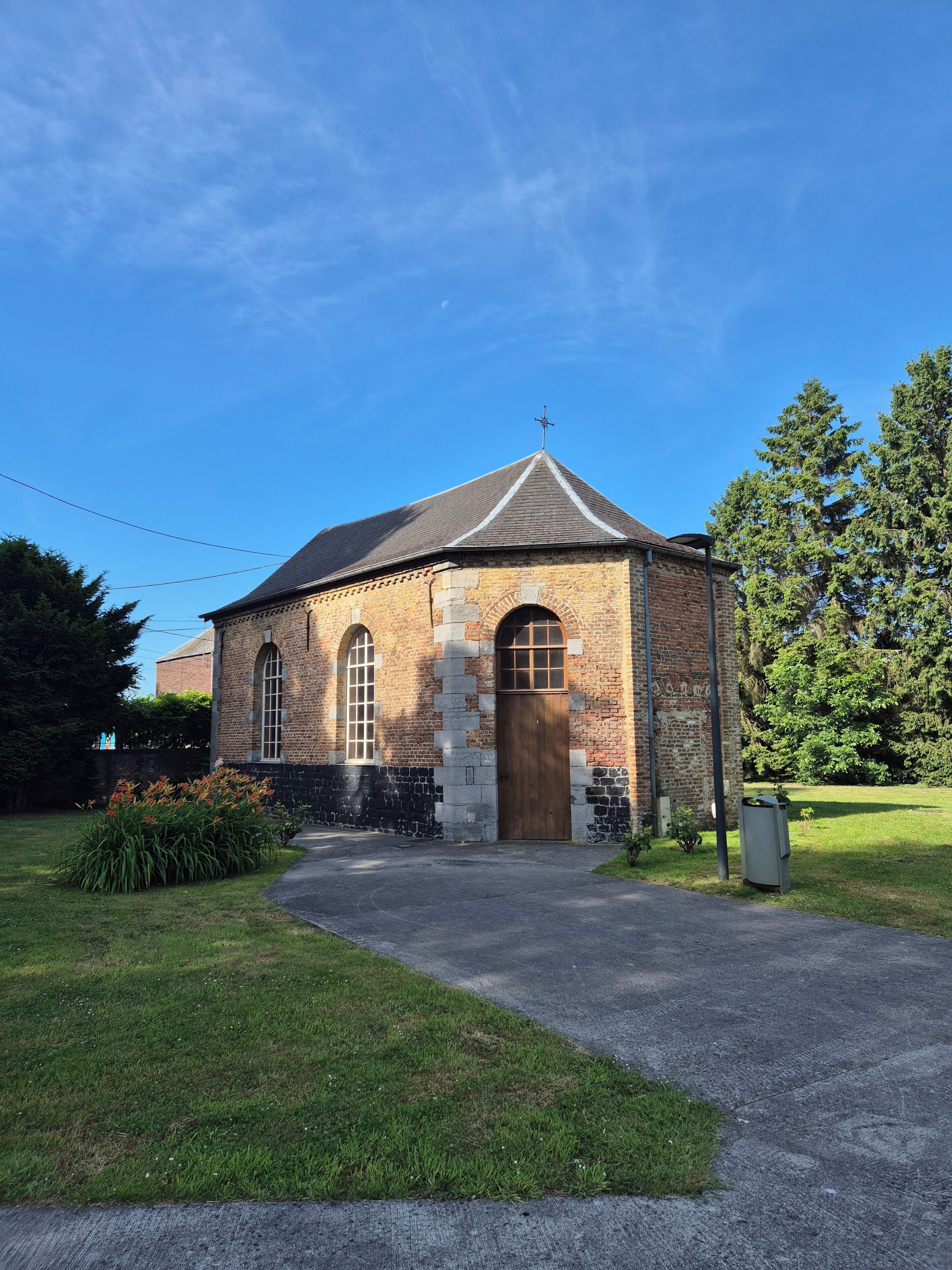 A small brick building with a pitched roof, a cross on top, and a single entrance.