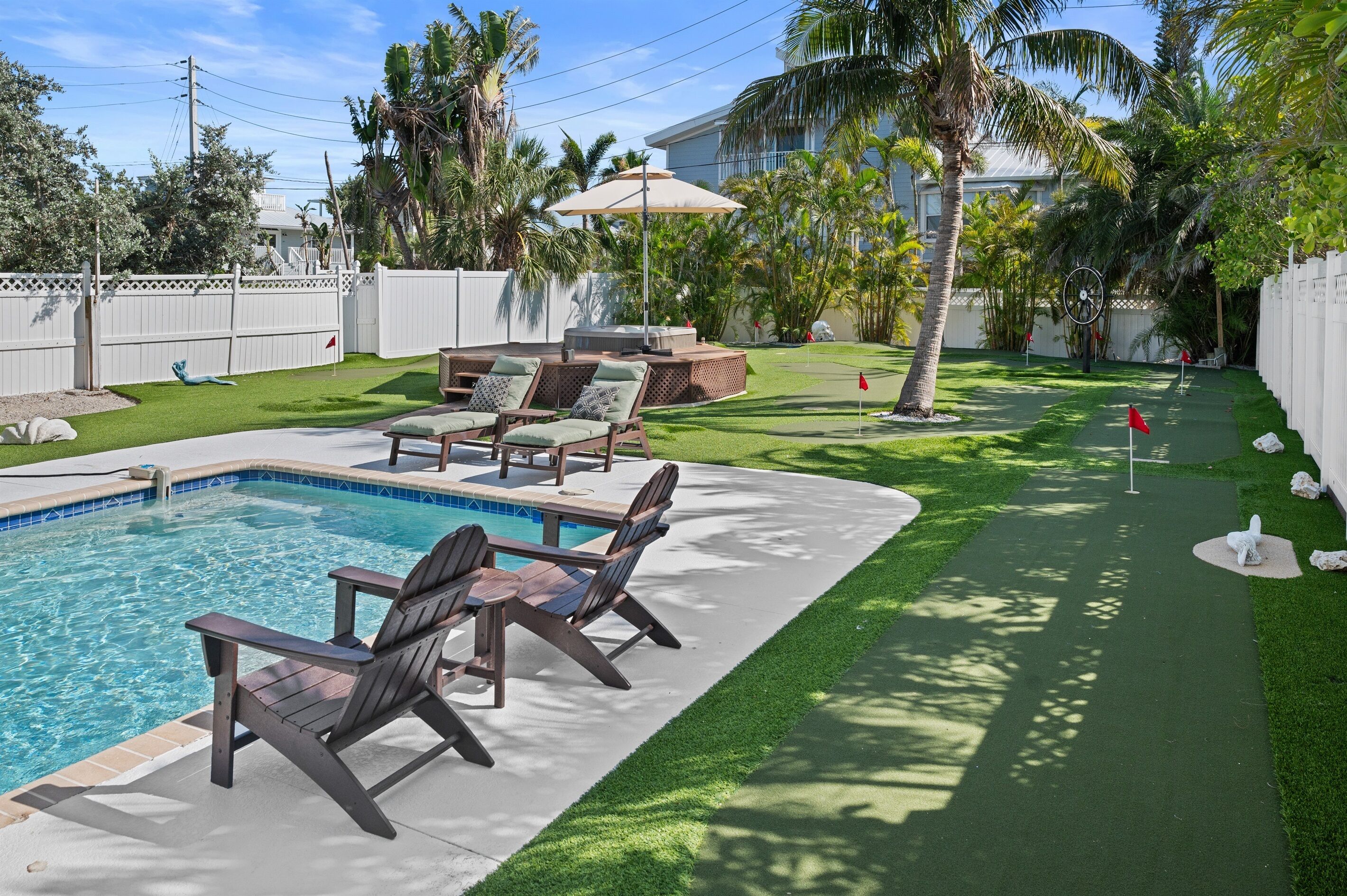 A backyard with a swimming pool, lounge chairs, a hot tub, and a small putting green.