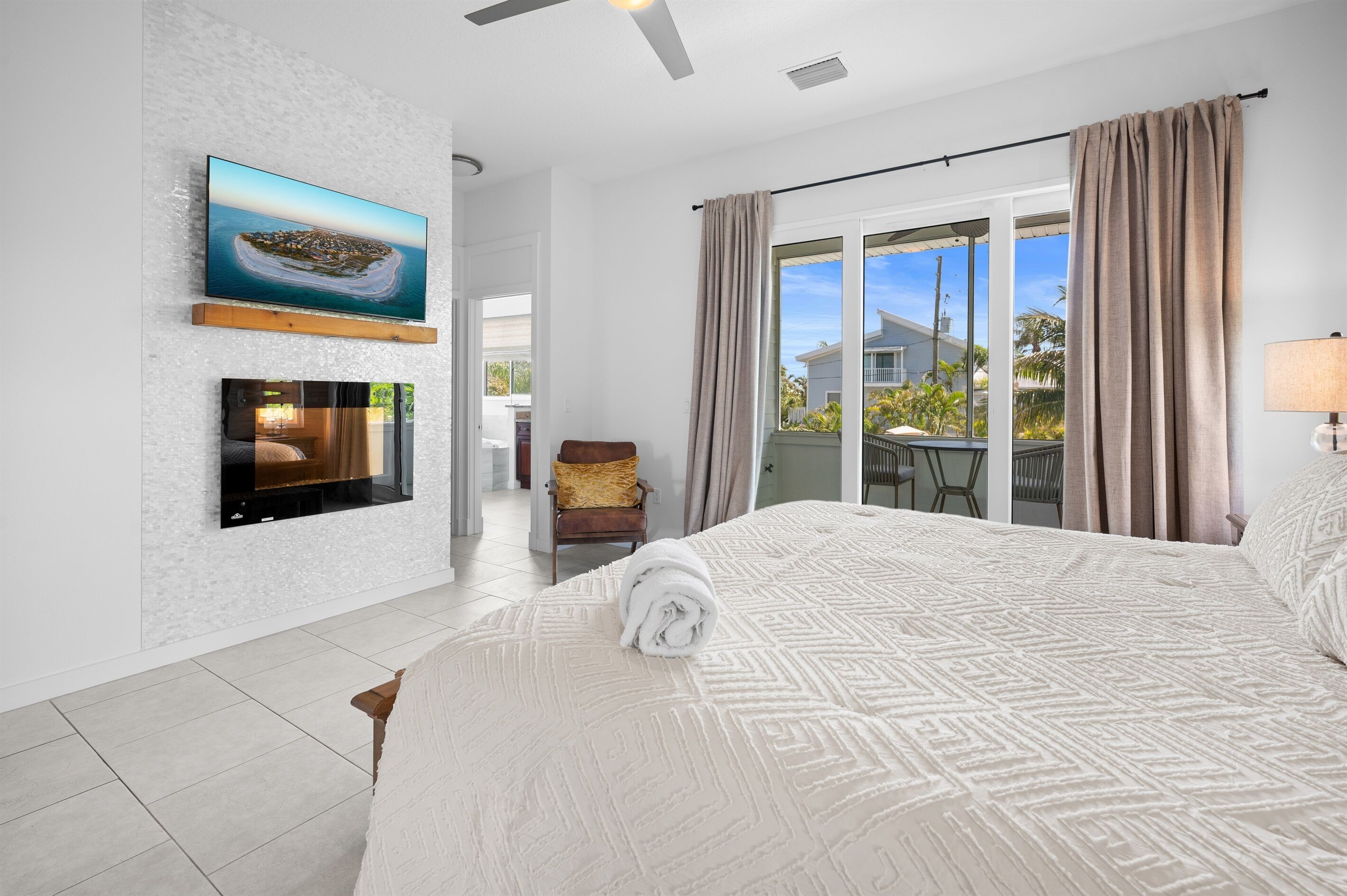Une chambre d’hôtel moderne dotée d’un grand lit, d’un téléviseur à écran plat fixé au mur, d’une cheminée et d’un balcon avec des rideaux.