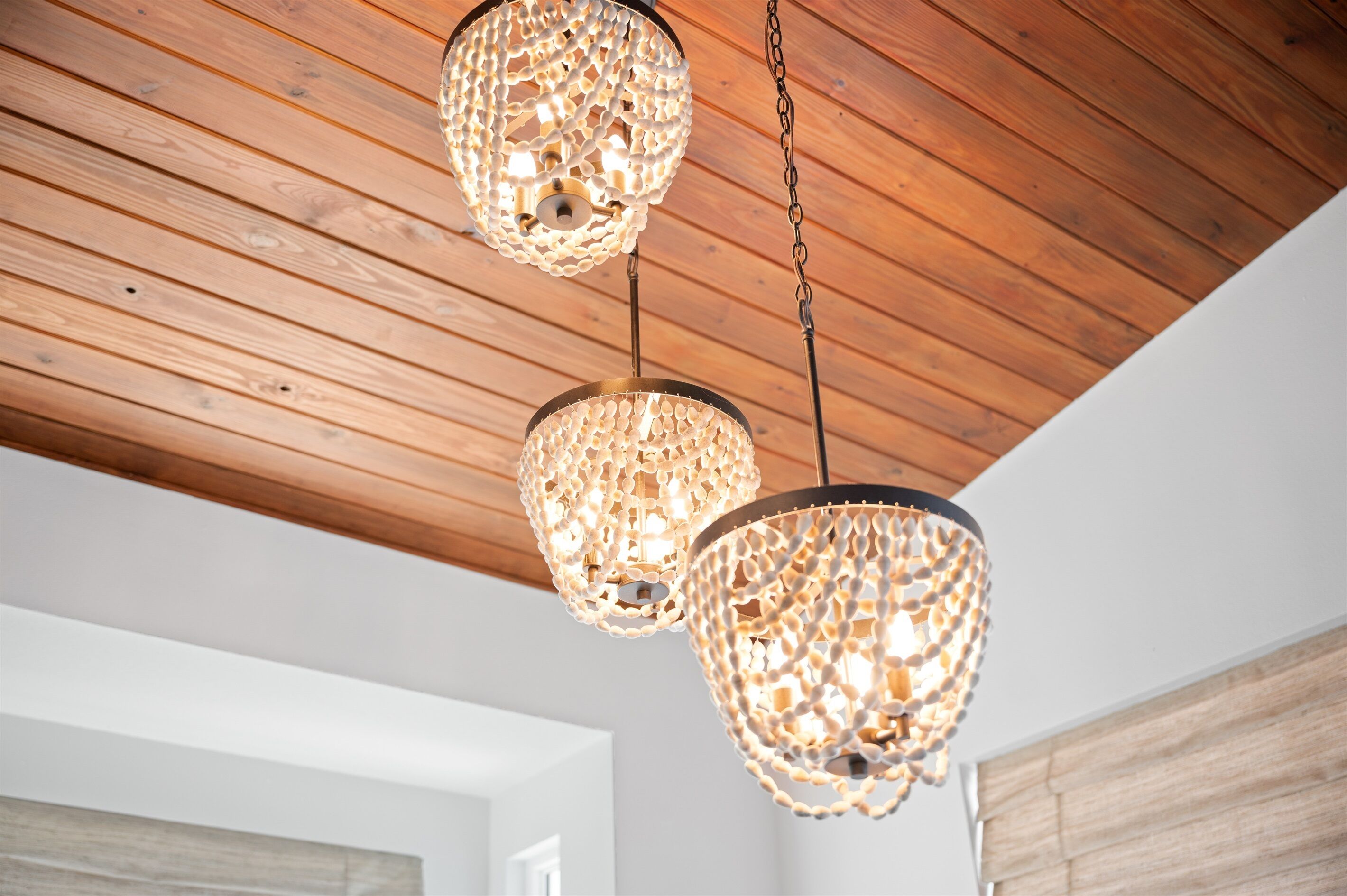 Trois suspensions décoratives, dotées d’un motif en treillis texturé, sont suspendues au plafond en bois.