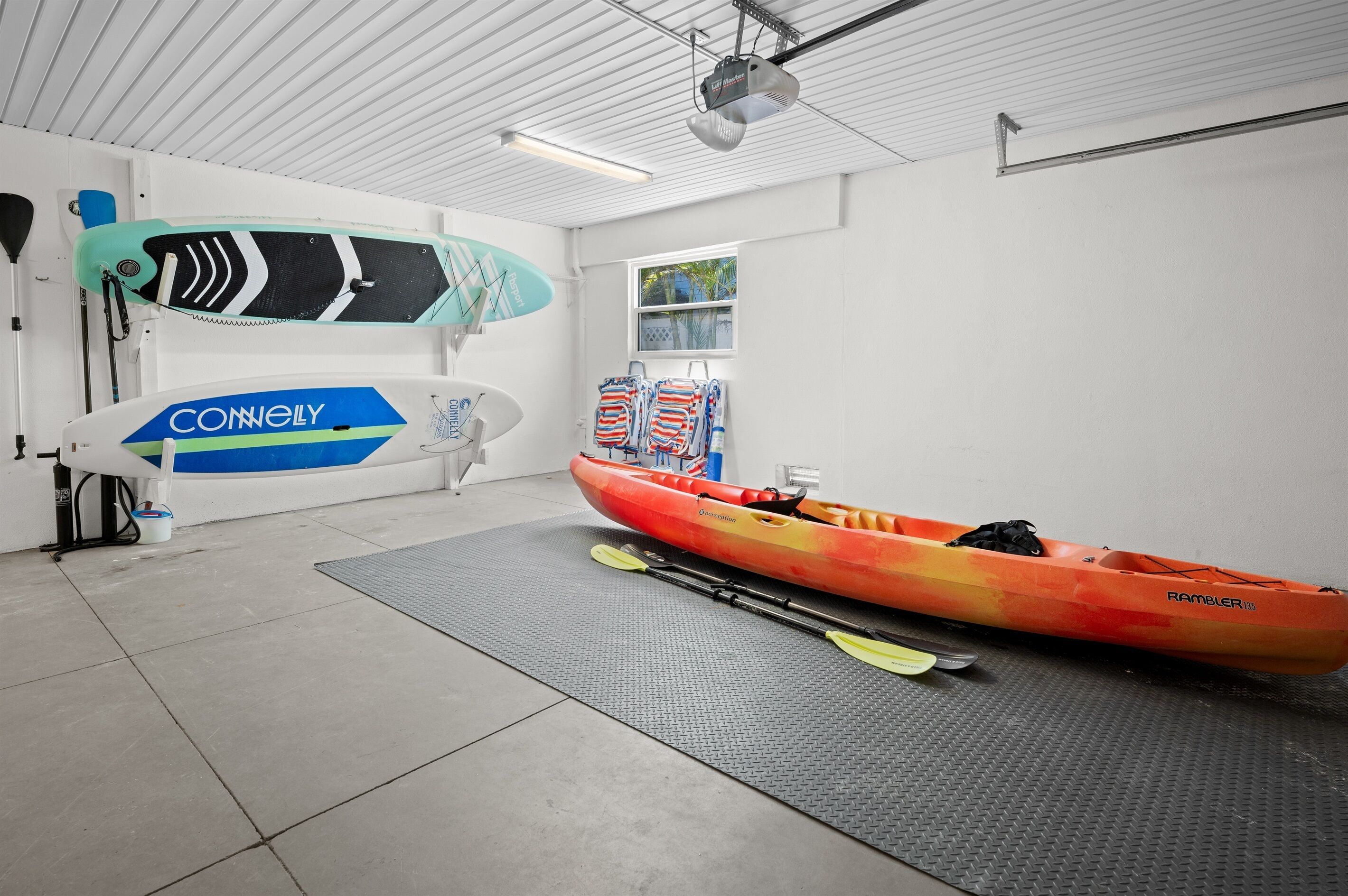A kayak and paddle in a room with a white ceiling and walls, a window, and a mat on the floor.