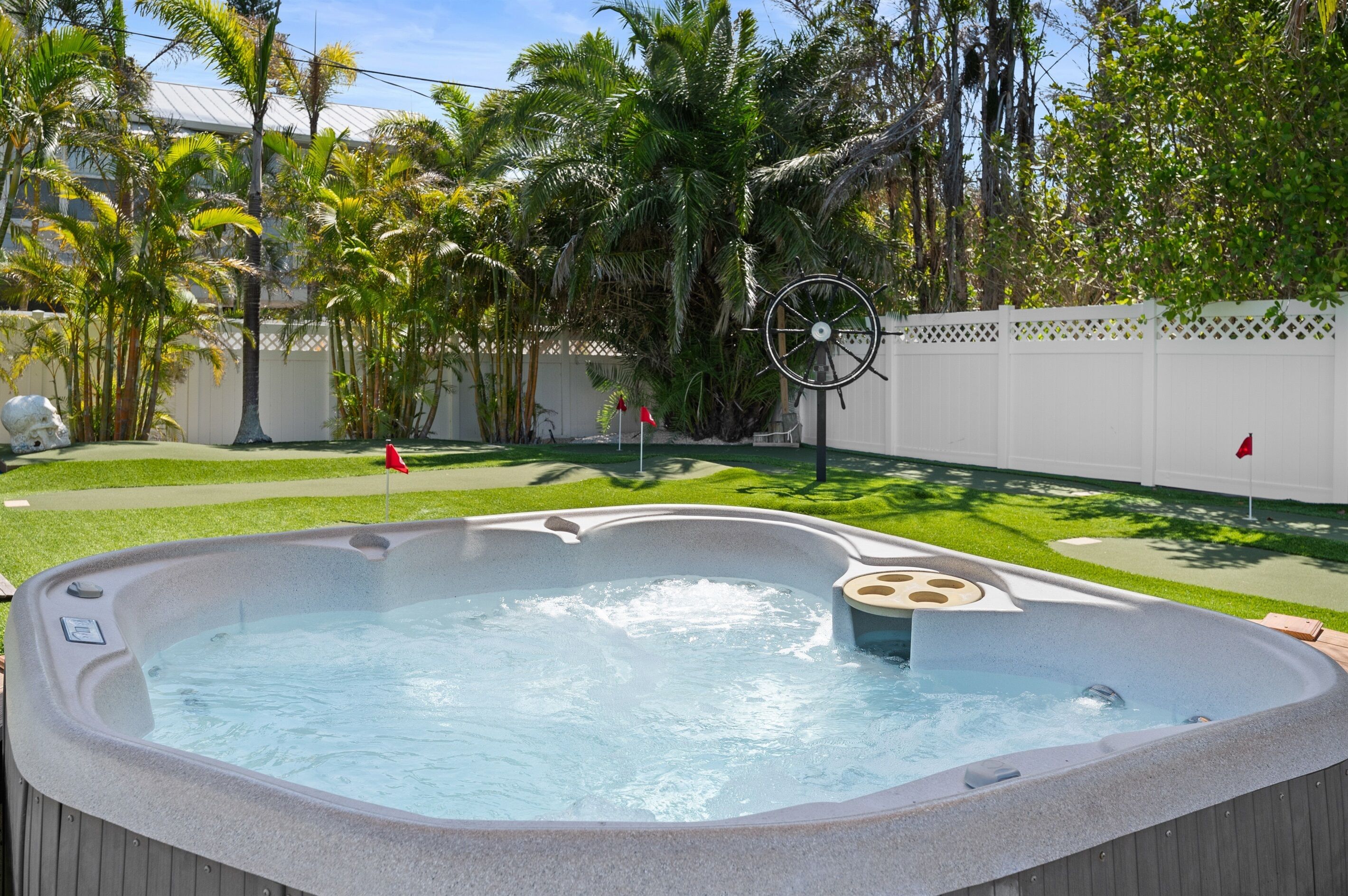 Ein Whirlpool in einem Garten mit weißem Zaun, Palmen und Rasen.