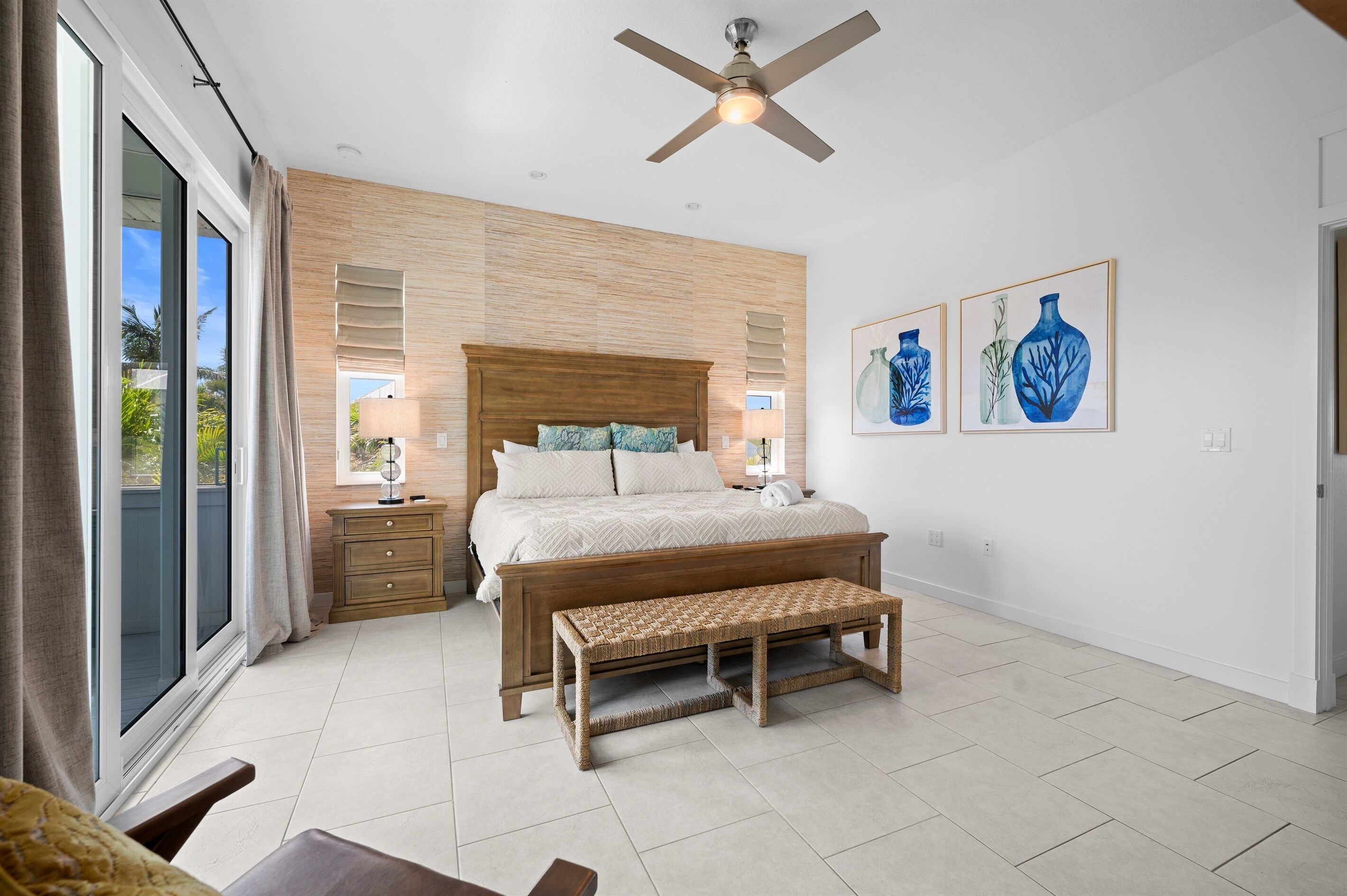 Une chambre à coucher avec un grand lit, une tête de lit en bois, un banc, une table de chevet et une fenêtre avec des rideaux.