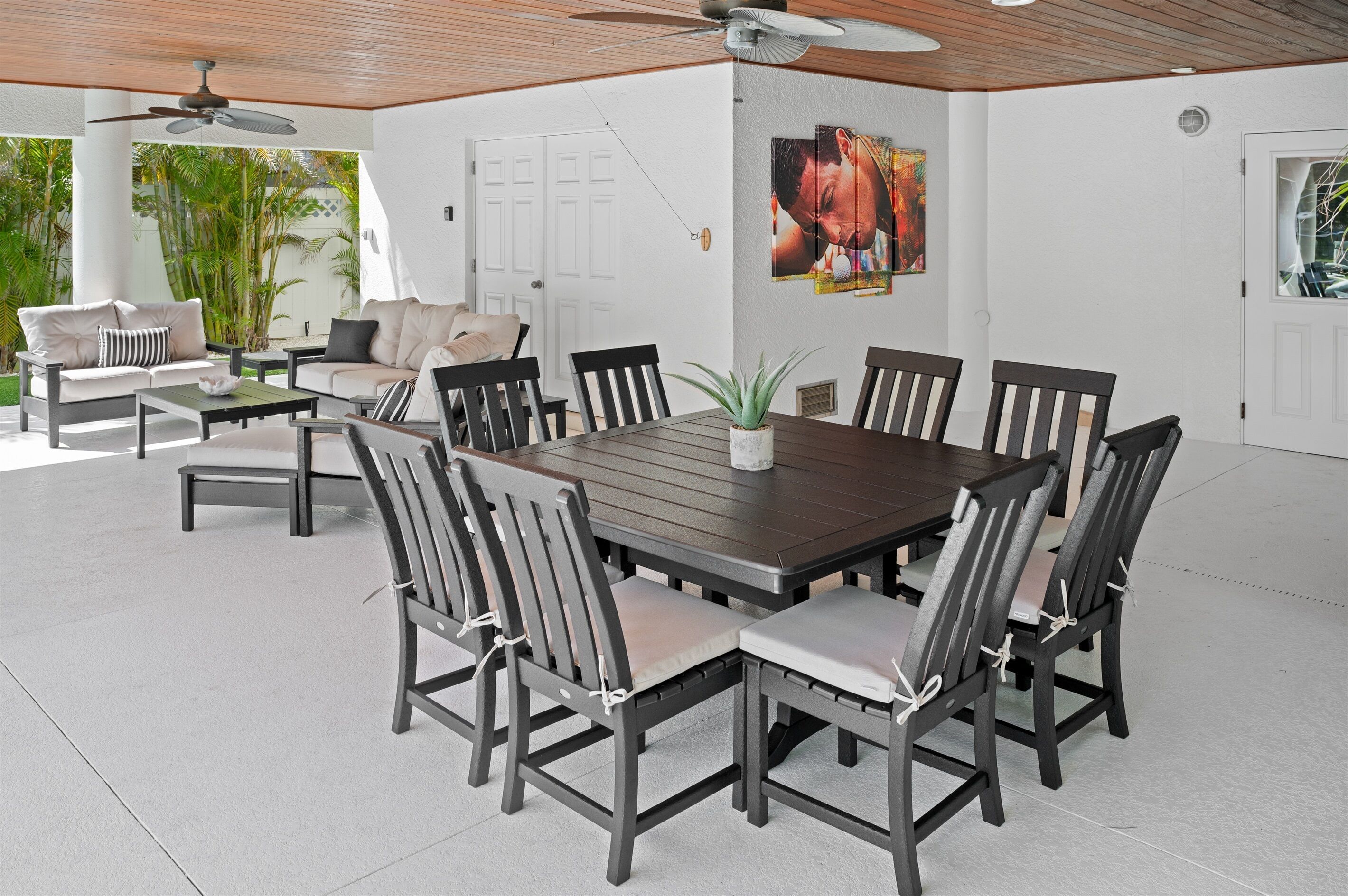 Un amplio patio con una mesa de comedor rodeada de sillas, un ventilador de techo y un gran ventanal con vistas a la vegetación.