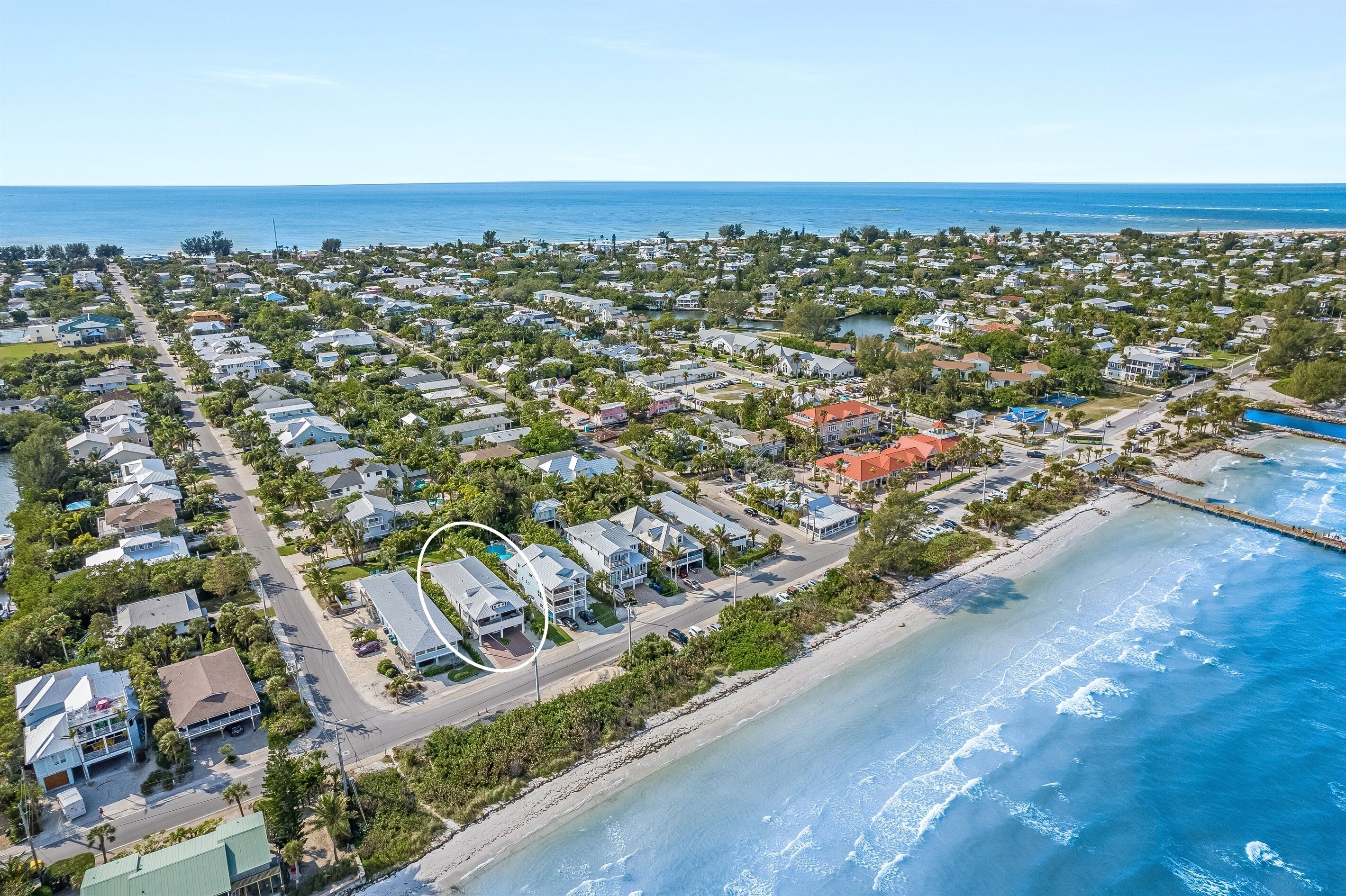 An aerial view of a coastal residential area with houses, a beach, and a pier.
