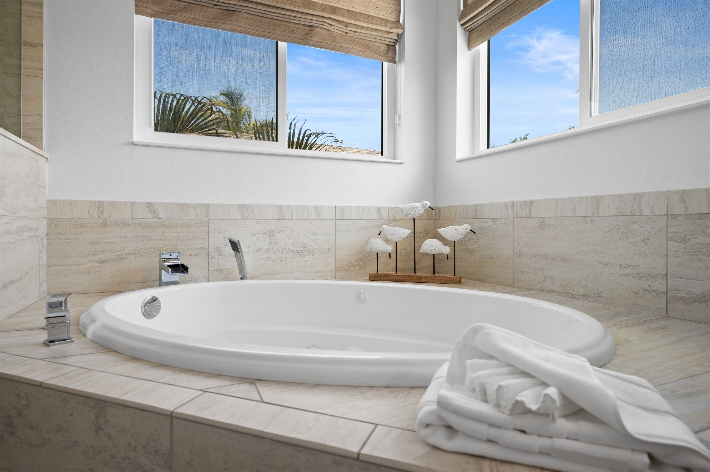 Ein modernes Badezimmer mit einer großzügigen Badewanne, einem Fenster mit Blick auf Palmen und einem Handtuchhalter mit Vogelzierde.