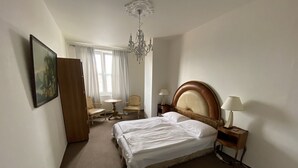 Et hotelværelse med en stor seng, to sengeborde med lamper, en lysekrone, et skrivebord med stol og et billede på væggen.