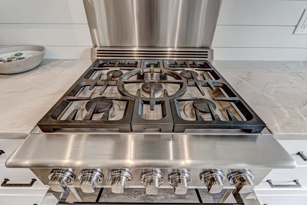 En gasblus i rustfrit stål med fire brændere og et kontrolpanel med drejeknapper.