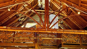 Interior rústico de una cabaña con techo de madera, una cama, una zona de cocina y una escalera.