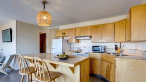A modern kitchen with wooden cabinets, a central island with bar stools, a refrigerator, a stove, and a microwave. - Ocean Front Duplex with Views! Dog Friendly! Free Wifi! (South Beach)