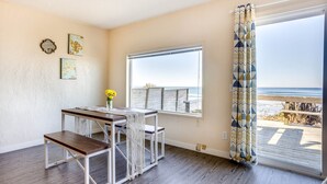 A room with a wooden floor, a table with a bench, a window with a view of the beach, and a curtain with a geometric pattern. - Ocean Front Duplex with Views! Dog Friendly! Free Wifi! (South Beach)