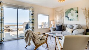 A living room with a sofa, armchairs, a coffee table, and a view of the beach. - Ocean Front Duplex with Views! Dog Friendly! Free Wifi! (South Beach)