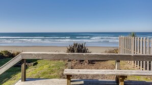 A wooden bench overlooking a beach with waves, a wooden fence, and a clear sky. - Ocean Front Duplex with Views! Dog Friendly! Free Wifi! (South Beach)