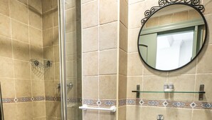 A bathroom with a glass-enclosed shower, a pedestal sink, a toilet, and a mirror with a decorative frame.