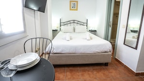 A neatly arranged hotel room with a bed, a chair, a table with plates and a glass, and a television on the wall.