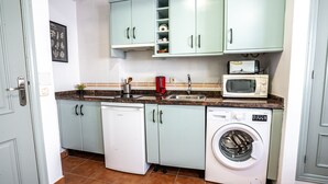 A compact kitchen with light green cabinets, a white dishwasher, a washing machine, a microwave, and a sink.