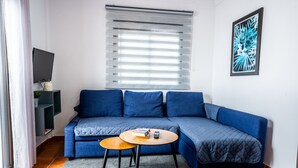 A modern living room with a blue sofa, a small round table, and a large window with blinds. - Marbella Village | Patio View Terrace (Marbella)