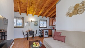 A cozy room with a wooden ceiling, a sofa, a dining table with chairs, a washing machine, and a kitchen area. - Marbella Village  | Appartment with Terrace (Marbella)