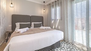 Een hotelkamer met een groot bed, een hoofdbord met een hondentandpatroon, twee hanglampen, dunne gordijnen en een vloer met dessin.