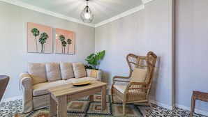 Een woonkamer met een bank, een rieten stoel, een salontafel en een kamerkleed met een patroon.