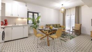 Eine moderne Küche mit weißen Schränken, einem Esstisch mit Stühlen, einer Couch und einem großen Fenster mit Vorhängen.