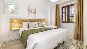 A neatly made bed with a green throw, a wall-mounted mirror, and a window with curtains. - Casa Castillo | Ground Floor Unit (Marbella)
