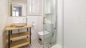 A bathroom with a wooden vanity, a white sink, a glass shower enclosure, and patterned floor tiles. - Casa Castillo | Ground Floor Unit (Marbella)