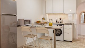 Cocina pequeña con refrigerador, microondas, lavamanos y lavadora. Hay dos sillas y una mesa con cosas para el desayuno.