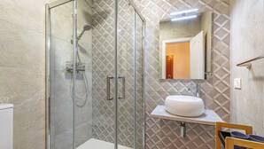 Un baño moderno con ducha de vidrio, lavamanos blanco y un espejo encima.