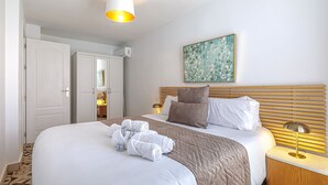 Una cama bien hecha con colcha marrón, almohadas blancas y cabecera de listones horizontales.