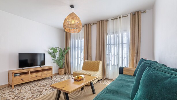 Una sala de estar con un sofá, un televisor sobre un mueble de madera, una mesa con fruteros y una lámpara colgante.