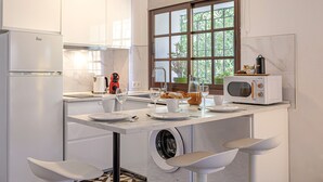 A compact kitchen with a built-in washing machine, a microwave, and a window with a view of greenery.