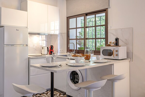 A compact kitchen with a built-in washing machine, a microwave, and a window with a view of greenery.