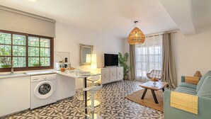 Un espacio habitable compacto con cocina, comedor y zona de estar, que presenta un piso estampado, lavadora, televisor y un ventanal grande.